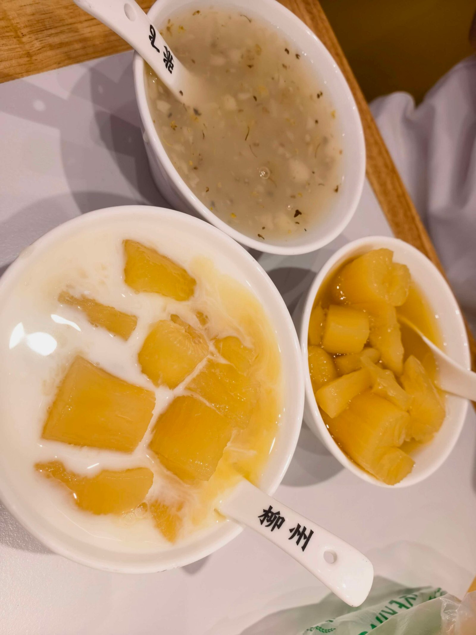 Three bowls of Chinese sweet soup desserts including jelly cubes and coconut milk on a Liuzhou street stall counter