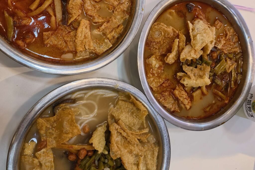 Three bowls of Liuzhou luosifen topped with fried tofu skin, peanuts and pickled bamboo shoots, seen from above