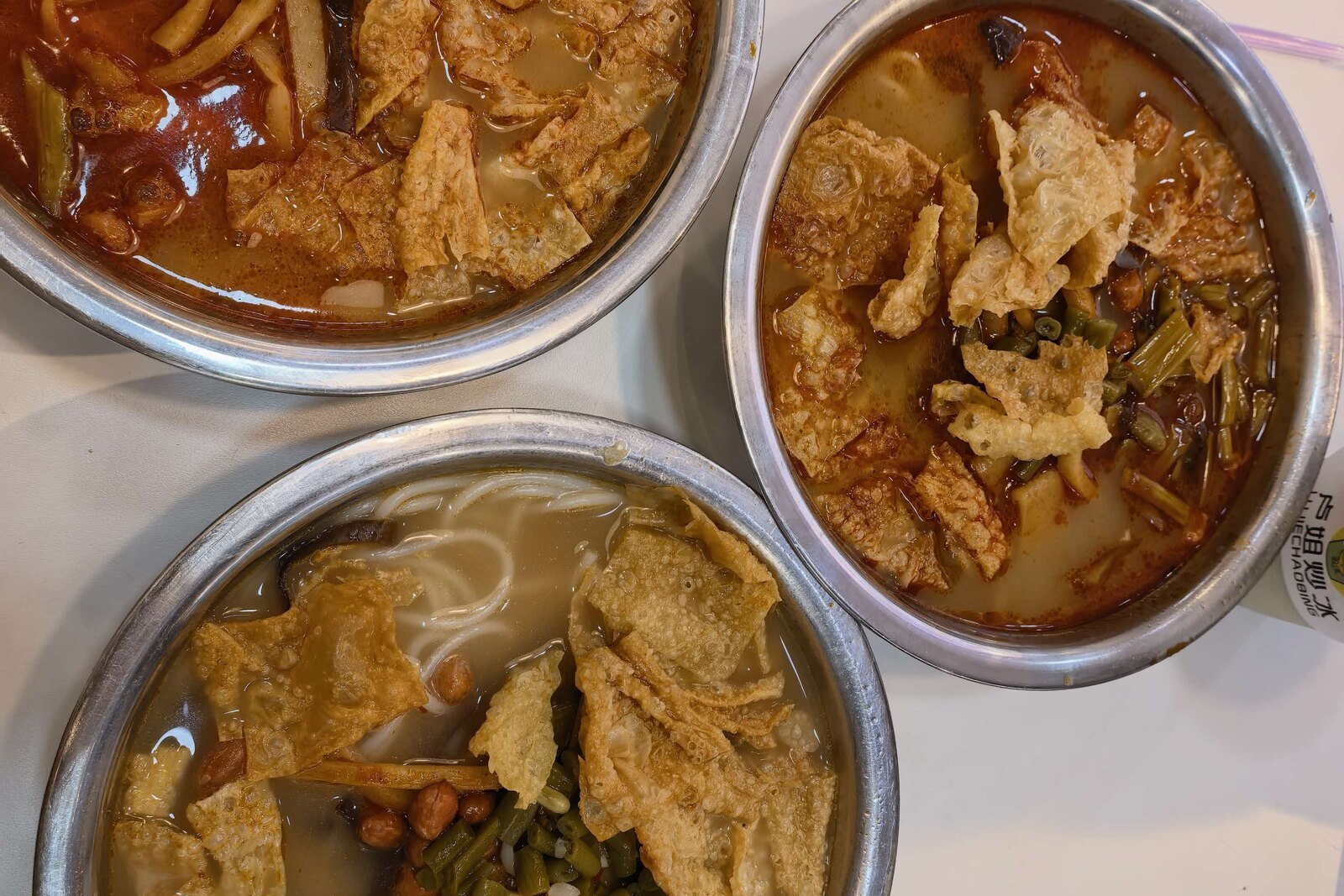 Three bowls of Liuzhou luosifen topped with fried tofu skin, peanuts and pickled bamboo shoots, seen from above