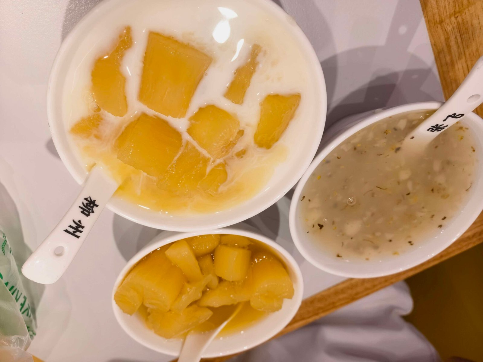 Three bowls of Chinese sweet soup desserts including jelly cubes and coconut milk on a Liuzhou street stall counter