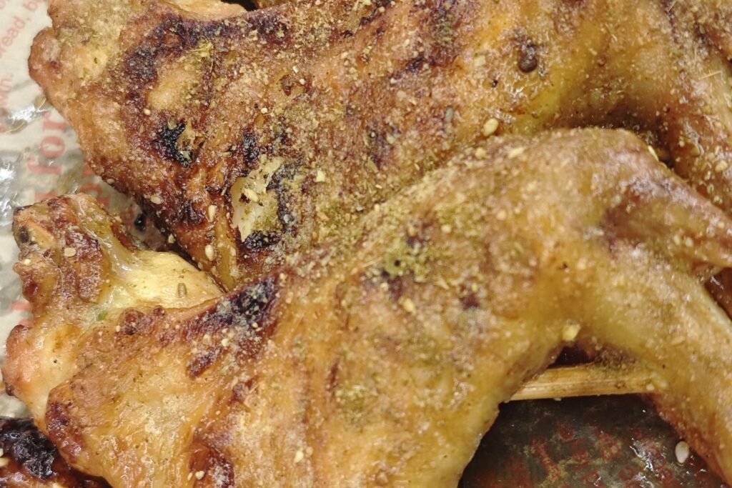 Close-up of charcoal-grilled chicken wings dusted with sesame and spices at a Zhanjiang late-night barbecue stall