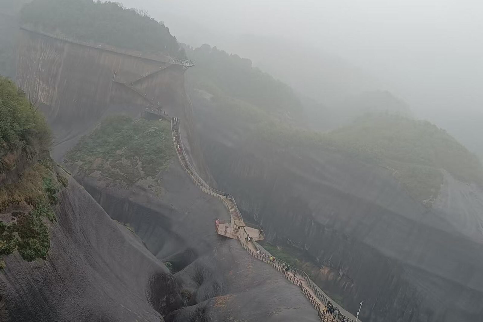 Fog rolling through the guardrail-lined walkway along the Gaoyi Ridge cliff edge