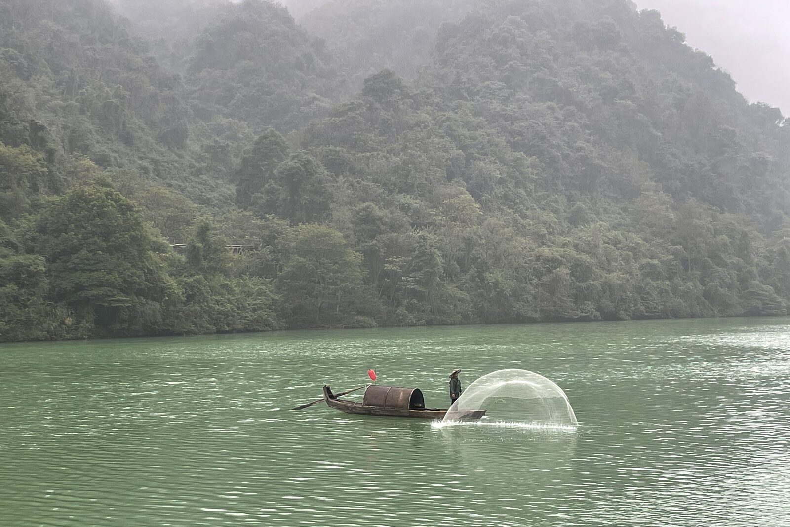 A wooden fishing boat on the misty jade-green water of Xiaodongjiang near Chenzhou